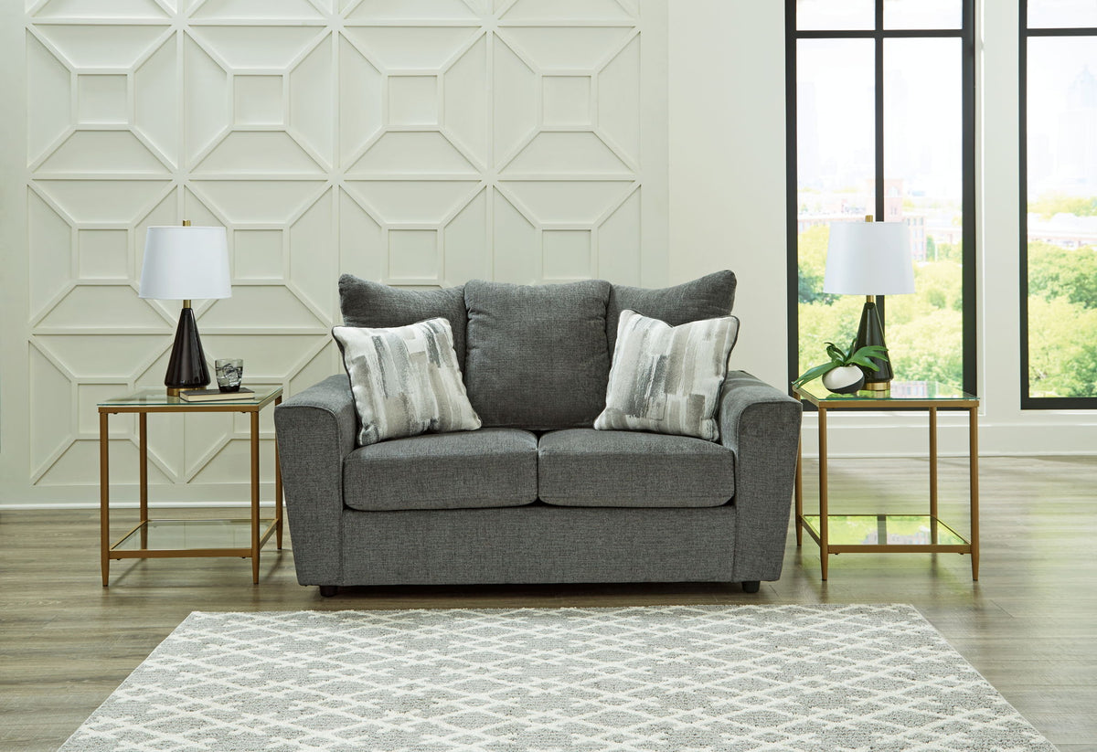 Gray sofa with patterned cushions in a living room setting with geometric wall design and large windows.