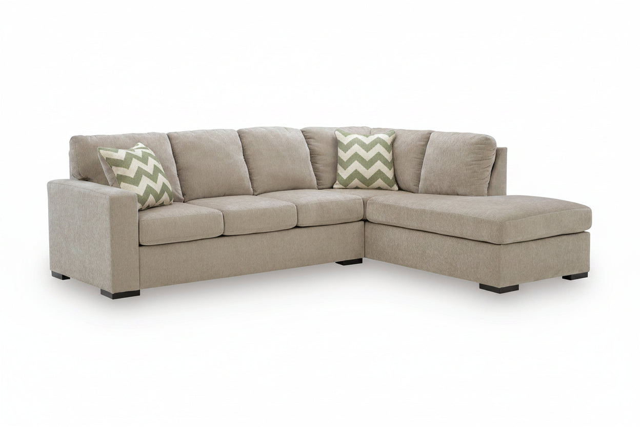 A light beige upholstered sectional sofa with a right-facing chaise lounge and two decorative throw pillows, shown on a clean white background.