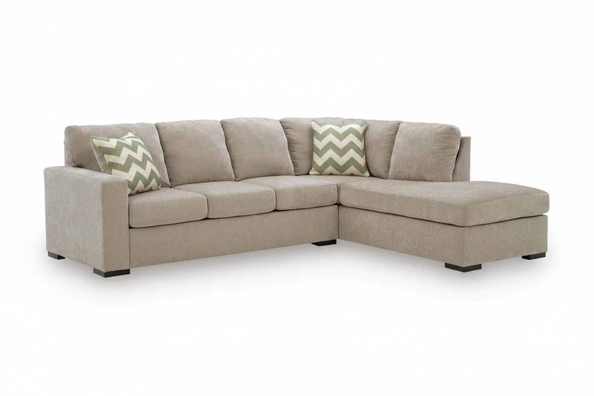A light beige upholstered sectional sofa with a right-facing chaise lounge and two decorative throw pillows, shown on a clean white background.