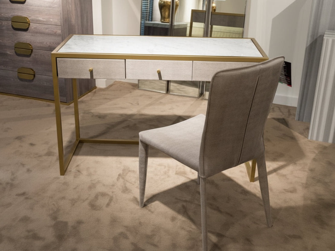 Modern desk with glass top and gold legs in a room setting
