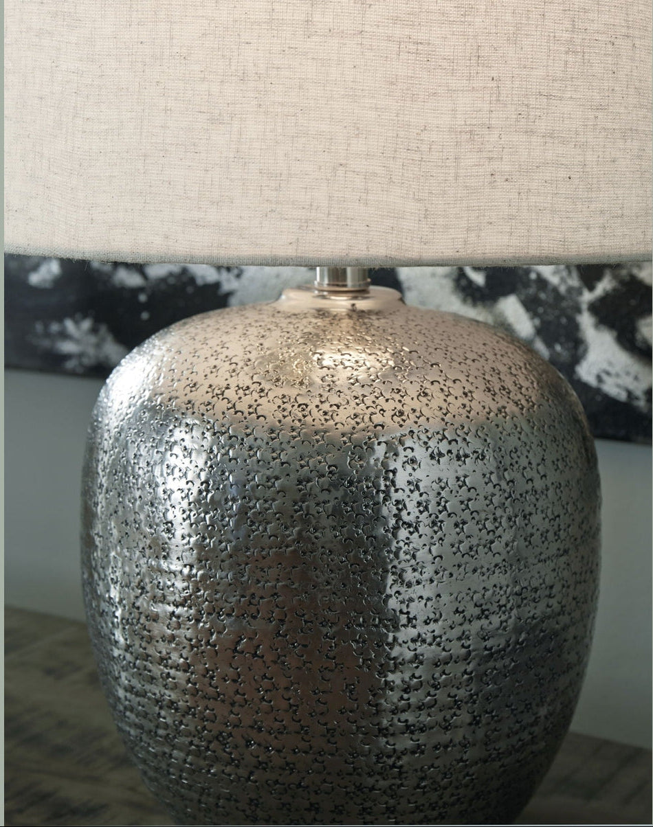 Table lamp with textured metallic base and beige lampshade on a neutral background
