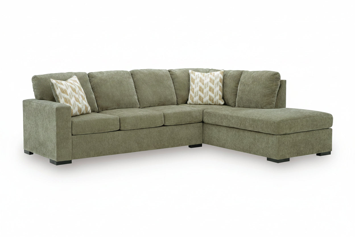 An L-shaped sectional sofa upholstered in textured sage green fabric, featuring two patterned throw pillows and black legs, shown on a white background.