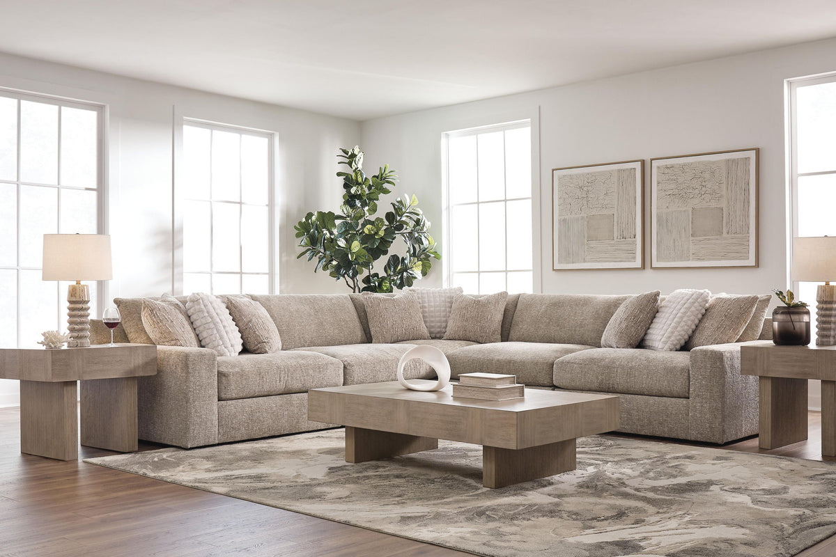 A light beige sectional sofa in a bright, modern living room with a matching wood coffee table, side tables, and a patterned area rug.