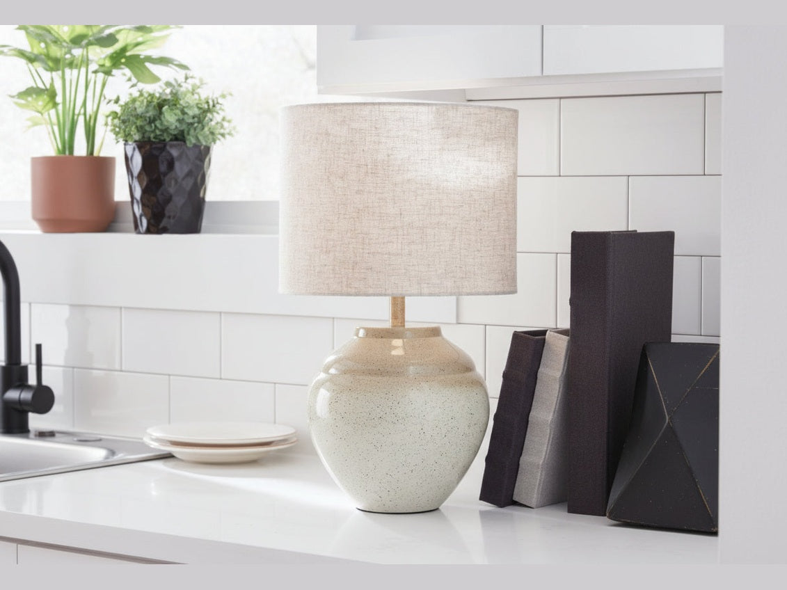 Waldish beige table lamp on a kitchen counter with plants and books in the background.