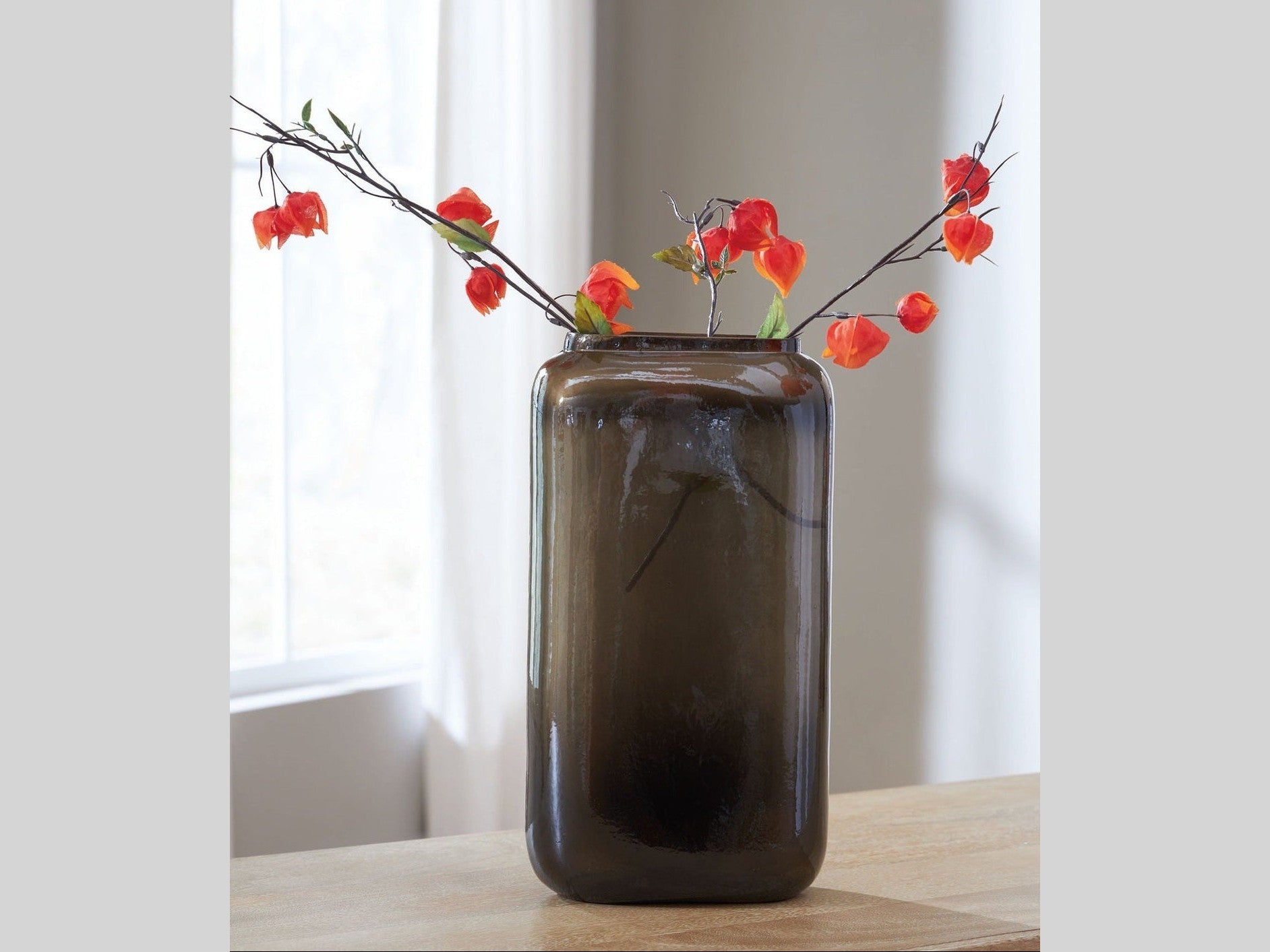 Dark glass vase with red flowers on a wooden surface