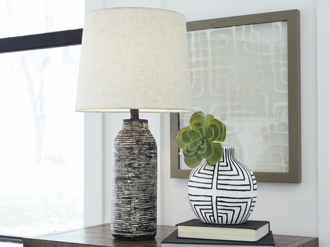 Mahima table lamp with textured base and white shade on a surface with decorative items.