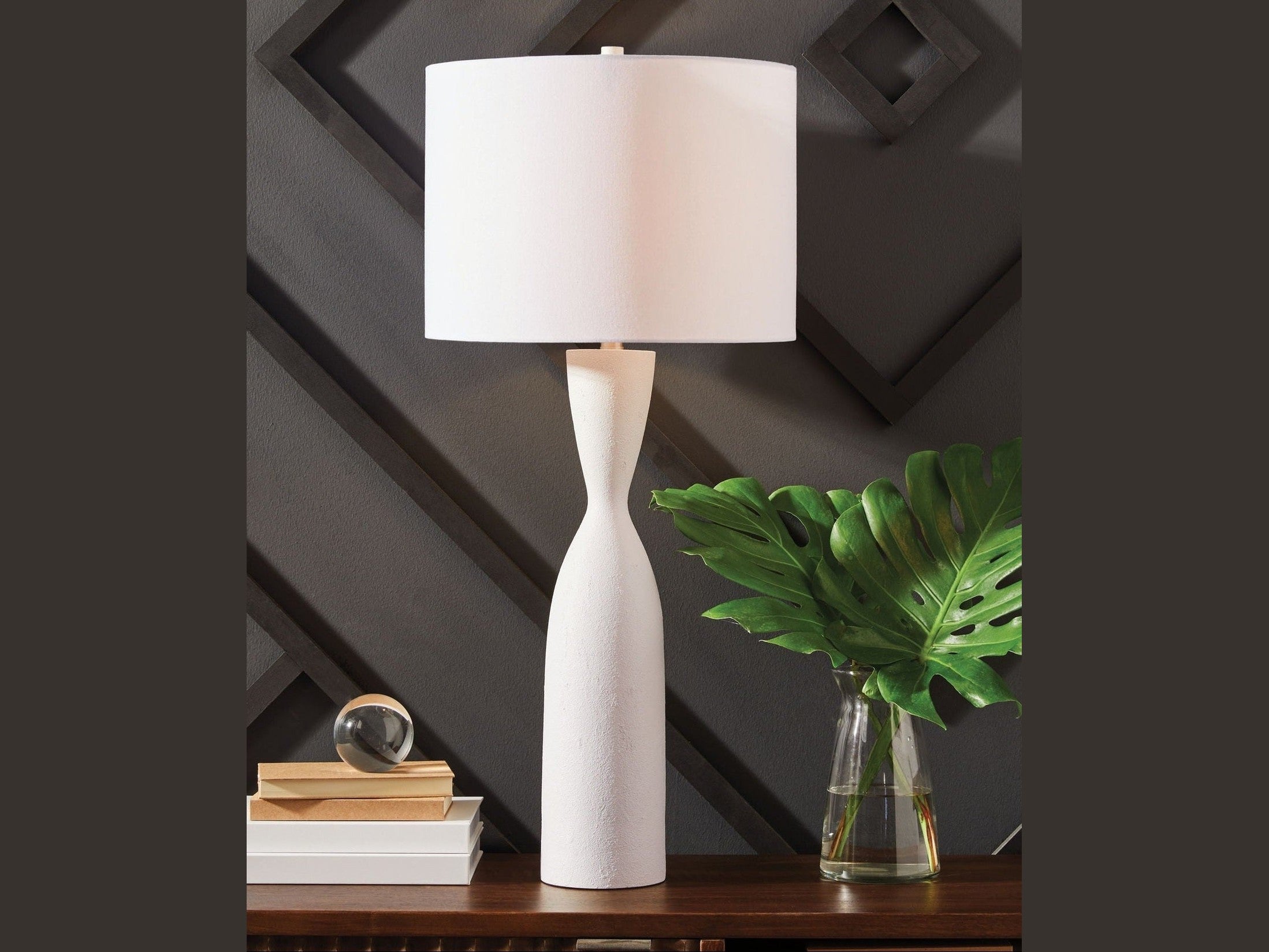 Davinford white table lamp on a wooden surface with decorative items against a dark wall.