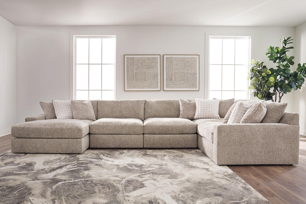 A light beige upholstered sectional sofa with matching throw pillows, shown in a bright, modern living room with wood floors, a patterned rug, and a potted plant.
