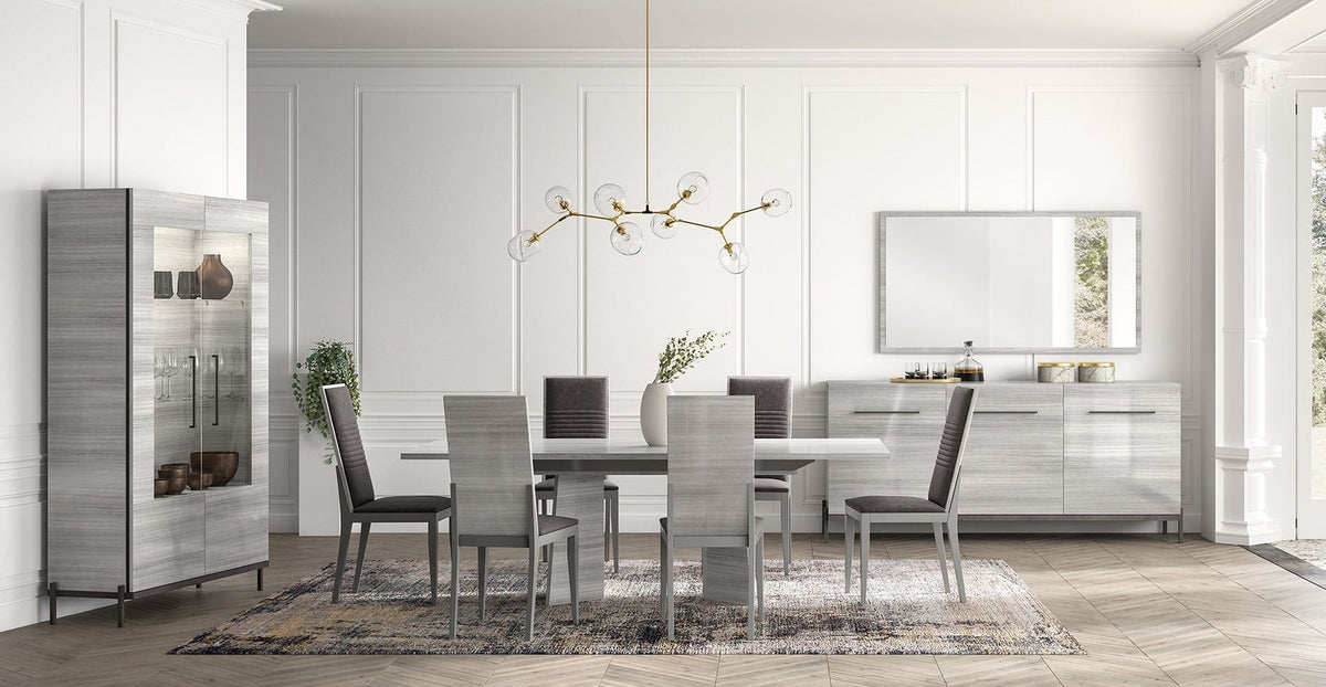 A modern dining room furniture set featuring a gray wood-grain dining table, six gray upholstered chairs, a tall matching gray side cabinet, a gray sideboard, and a gold multi-arm chandelier, all arranged on a patterned rug in a bright white paneled room.
