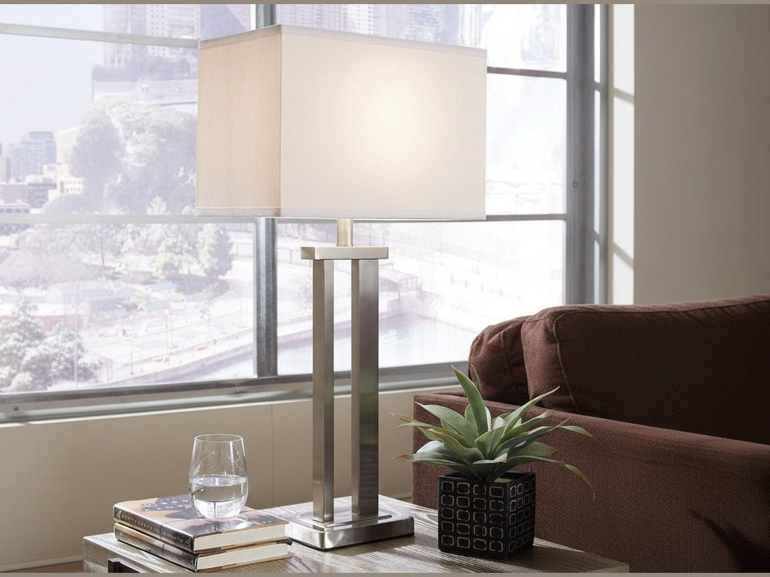 Aniela able lamp on a table with a glass of water and books in a room with large windows.