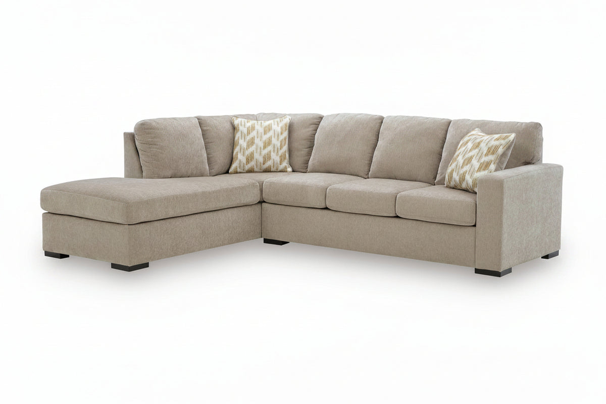 A light beige upholstered L-shaped corner sectional sofa with two patterned accent pillows, shown on a clean white background.
