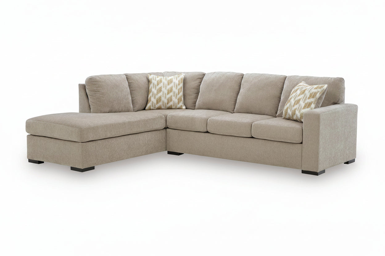 A light beige upholstered L-shaped corner sectional sofa with two patterned accent pillows, shown on a clean white background.