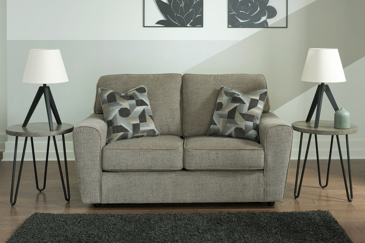 Gray sofa with patterned cushions in a living room setting with two side tables and lamps.