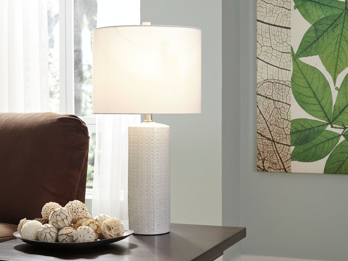 Steuben white textured table lamp on a surface with a decorative item and window in the background.