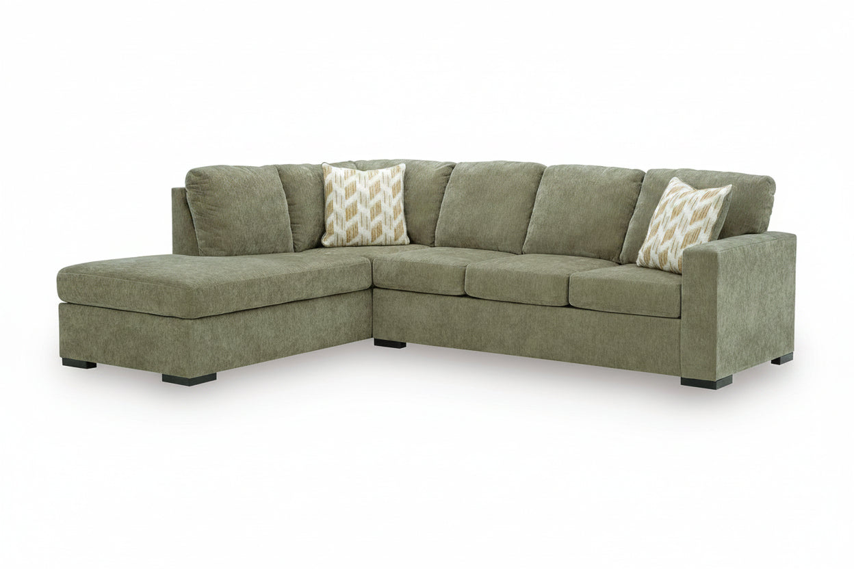 An L-shaped sectional sofa upholstered in textured sage green fabric, featuring two decorative throw pillows with a beige and white chevron pattern, set against a plain white background.