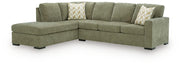 An L-shaped sectional sofa upholstered in textured sage green fabric, featuring two decorative throw pillows with a beige and white chevron pattern, set against a plain white background.