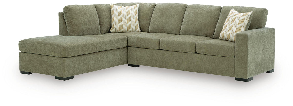 An L-shaped sectional sofa upholstered in textured sage green fabric, featuring two decorative throw pillows with a beige and white chevron pattern, set against a plain white background.