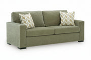 An olive green upholstered loveseat sofa with two patterned throw pillows, shown on a plain white background.