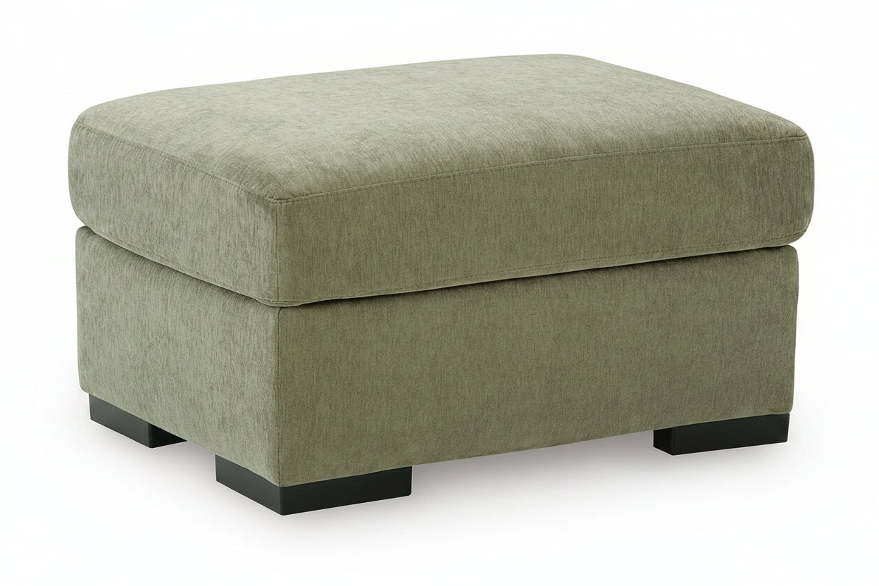 An upholstered square ottoman with a textured fabric in a muted sage green color and black block feet, shown on a plain white background.