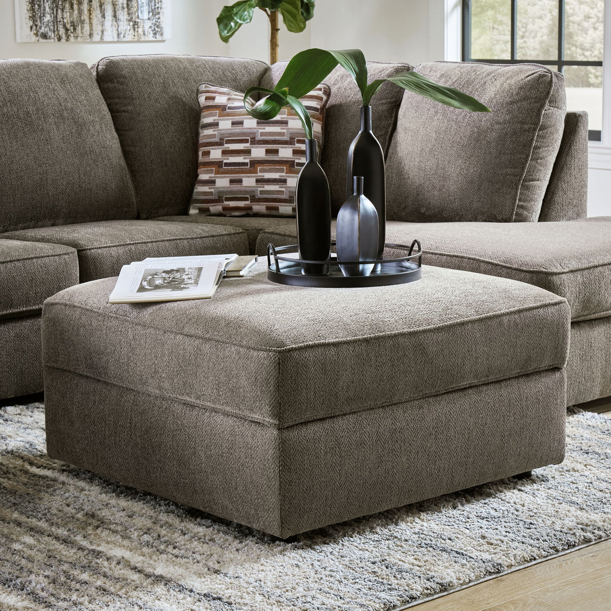Gray sectional sofa with ottoman and decorative items in a living room setting