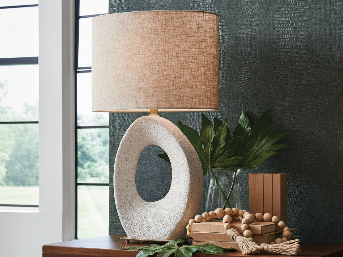 Trentlen decorative table lamp with a textured beige shade on a wooden surface near a window.