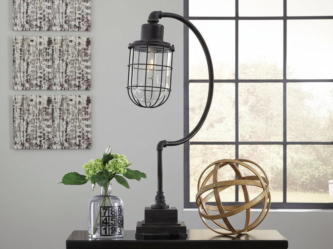 Jae vintage-style table lamp with a metal cage shade on a desk with decorative items.