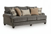 A three-seat upholstered sofa in dark gray fabric, styled with five throw pillows including two plaid and two solid beige and textured neutral designs, shown on a white background.