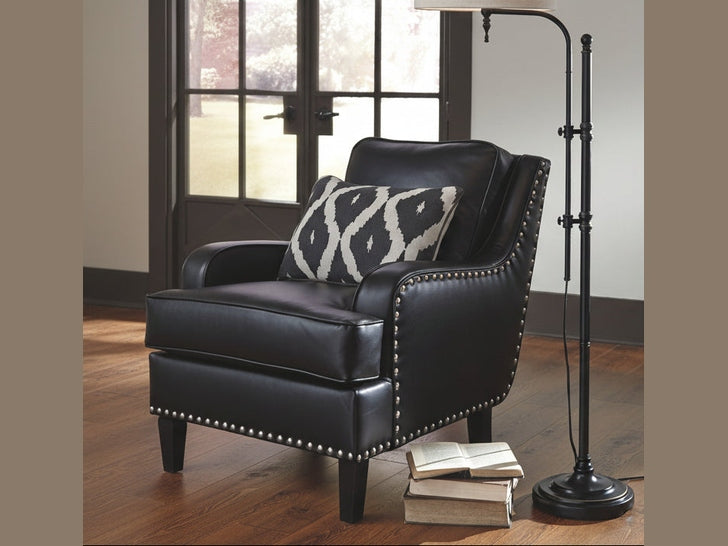 Black leather armchair with a patterned pillow next to a floor lamp in a room with a window.