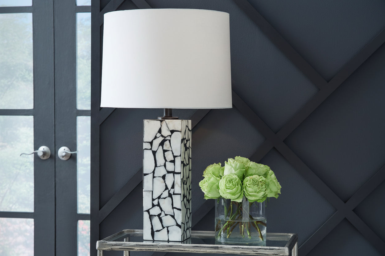 Table lamp with a mosaic design base next to a vase of green roses against a dark wall.