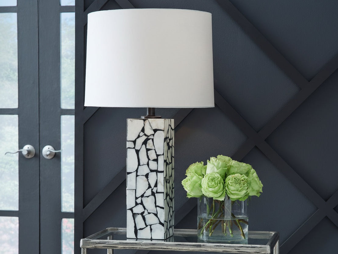 Table lamp with a mosaic design base next to a vase of green roses against a dark wall.