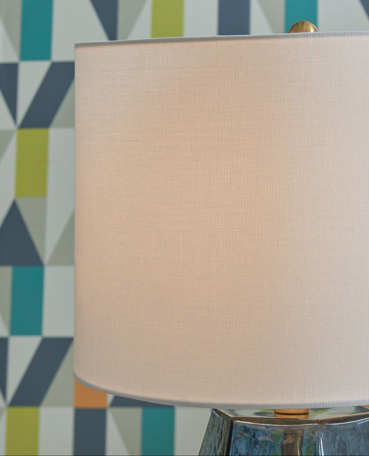 Beige lampshade on a metallic base against a geometric-patterned wall.