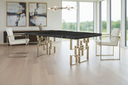 Dining table with geometric brass legs and two chairs in a room scene.
