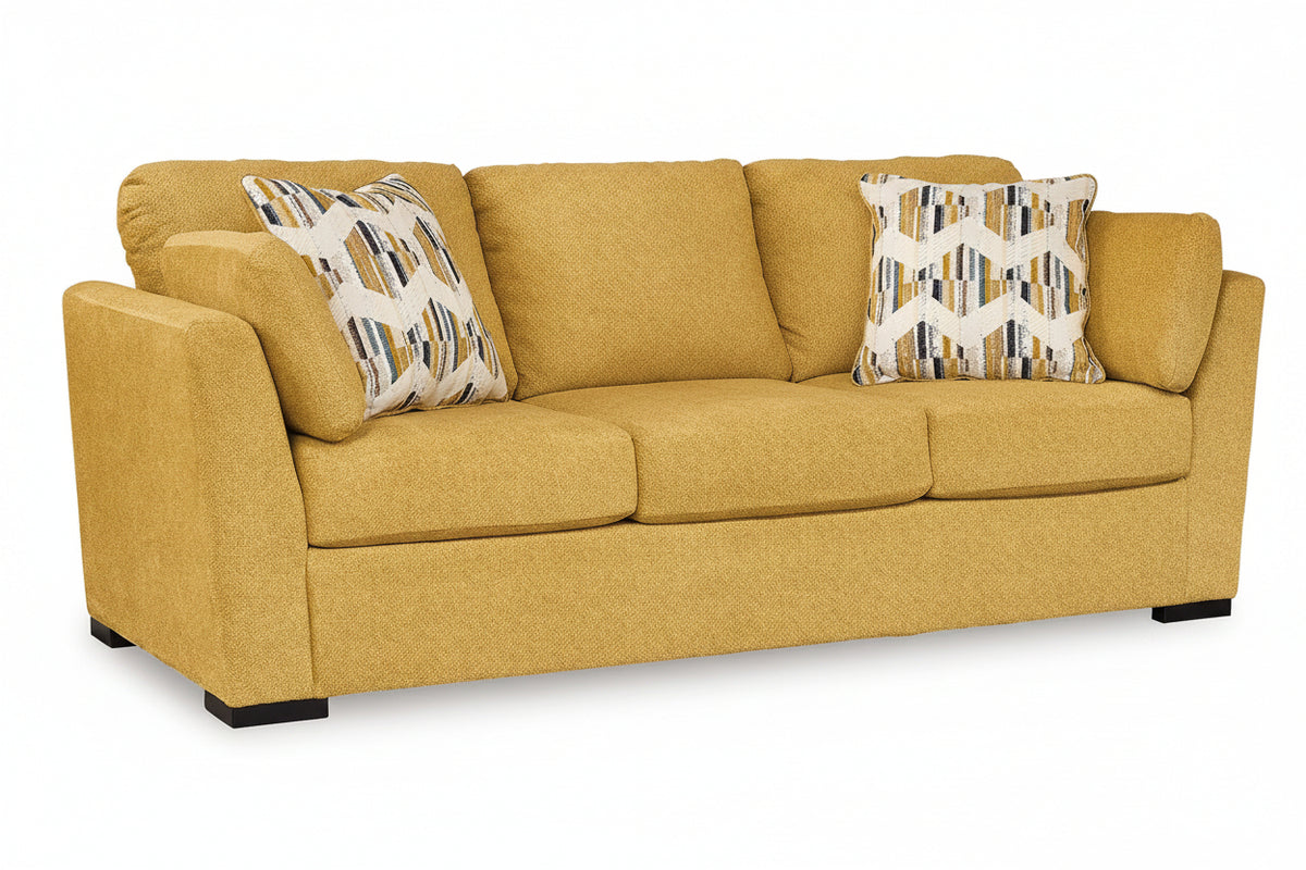 A three-seater sofa upholstered in textured mustard yellow fabric, featuring two decorative throw pillows with geometric patterns, set against a plain white background.