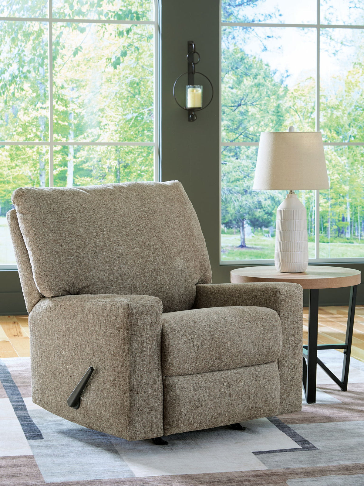 Beige recliner chair in a living room with large windows and a lamp.