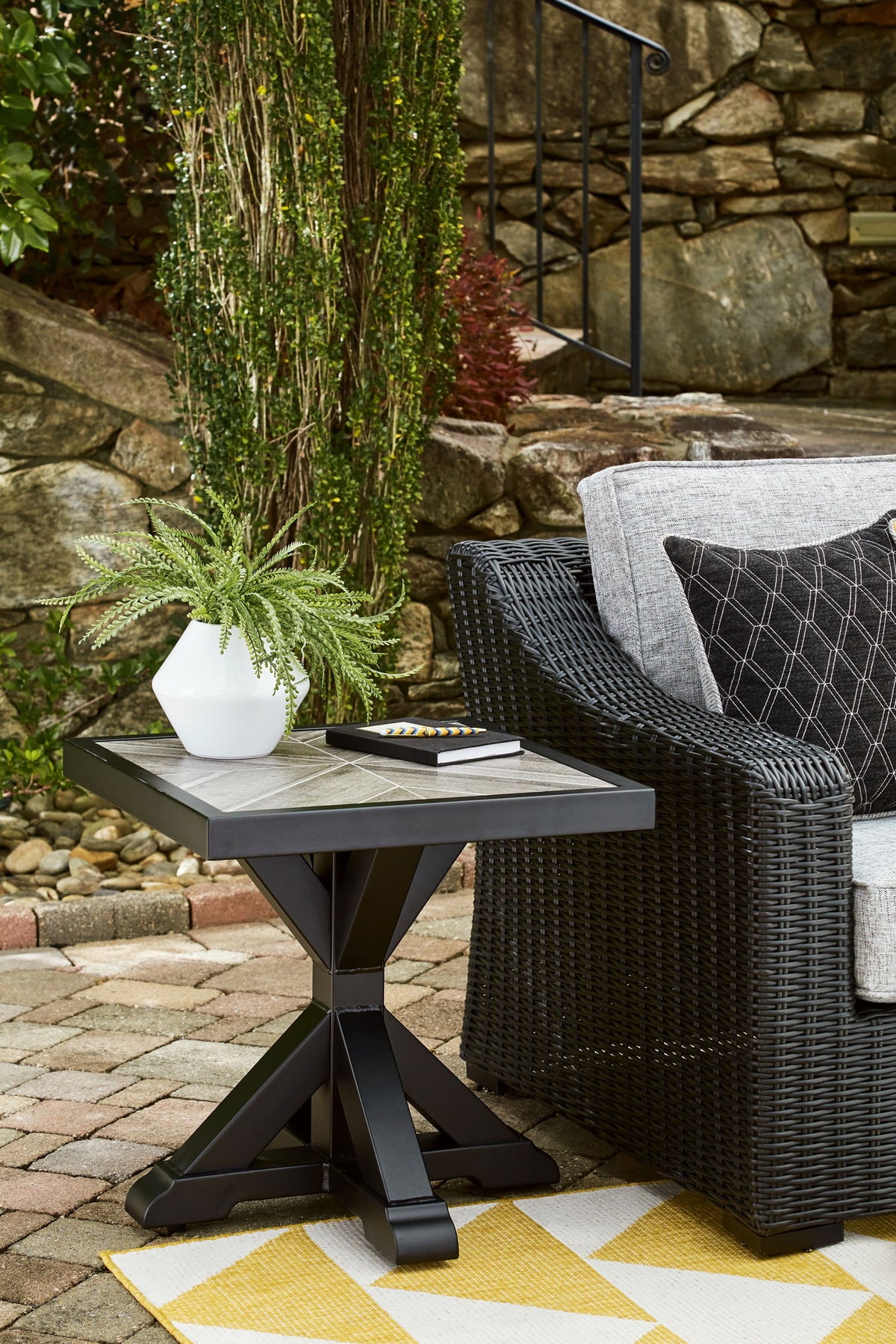 Outdoor patio setting with a black wicker chair and side table on a stone patio.