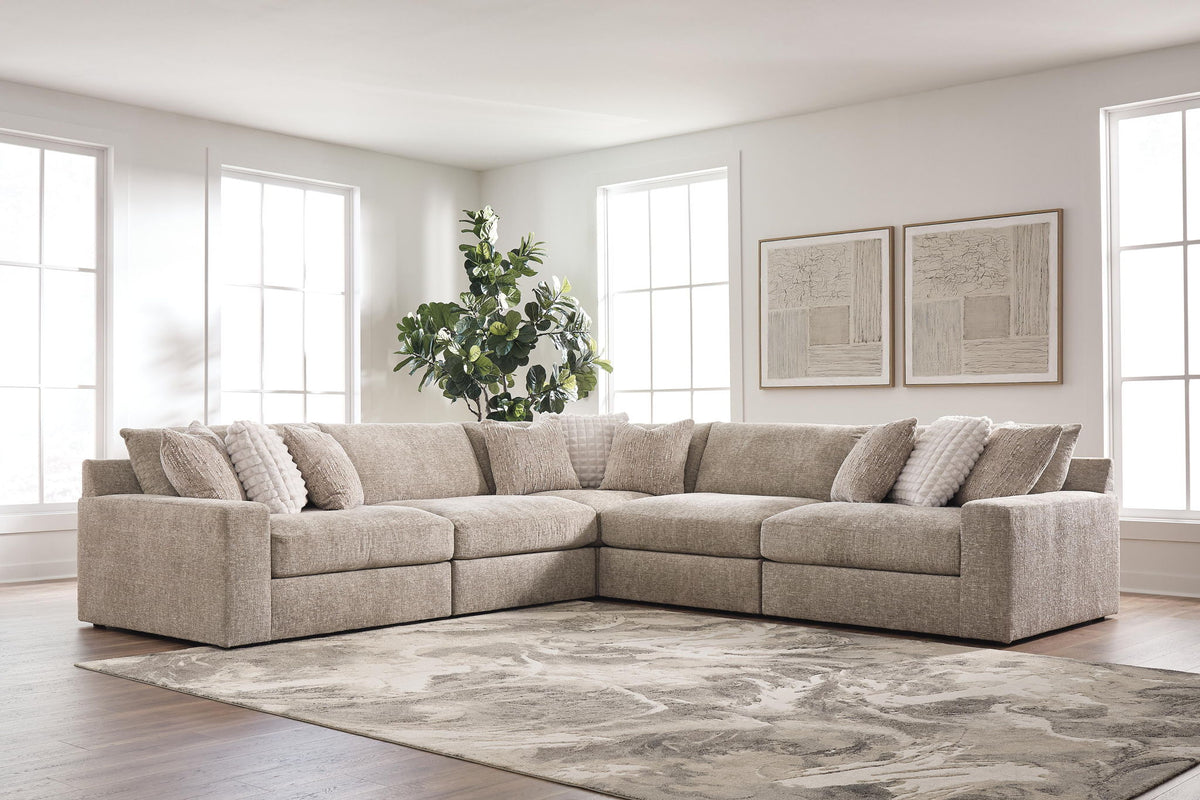 A light beige sectional sofa with matching throw pillows in a bright, modern living room with hardwood floors, a patterned rug, and large windows.