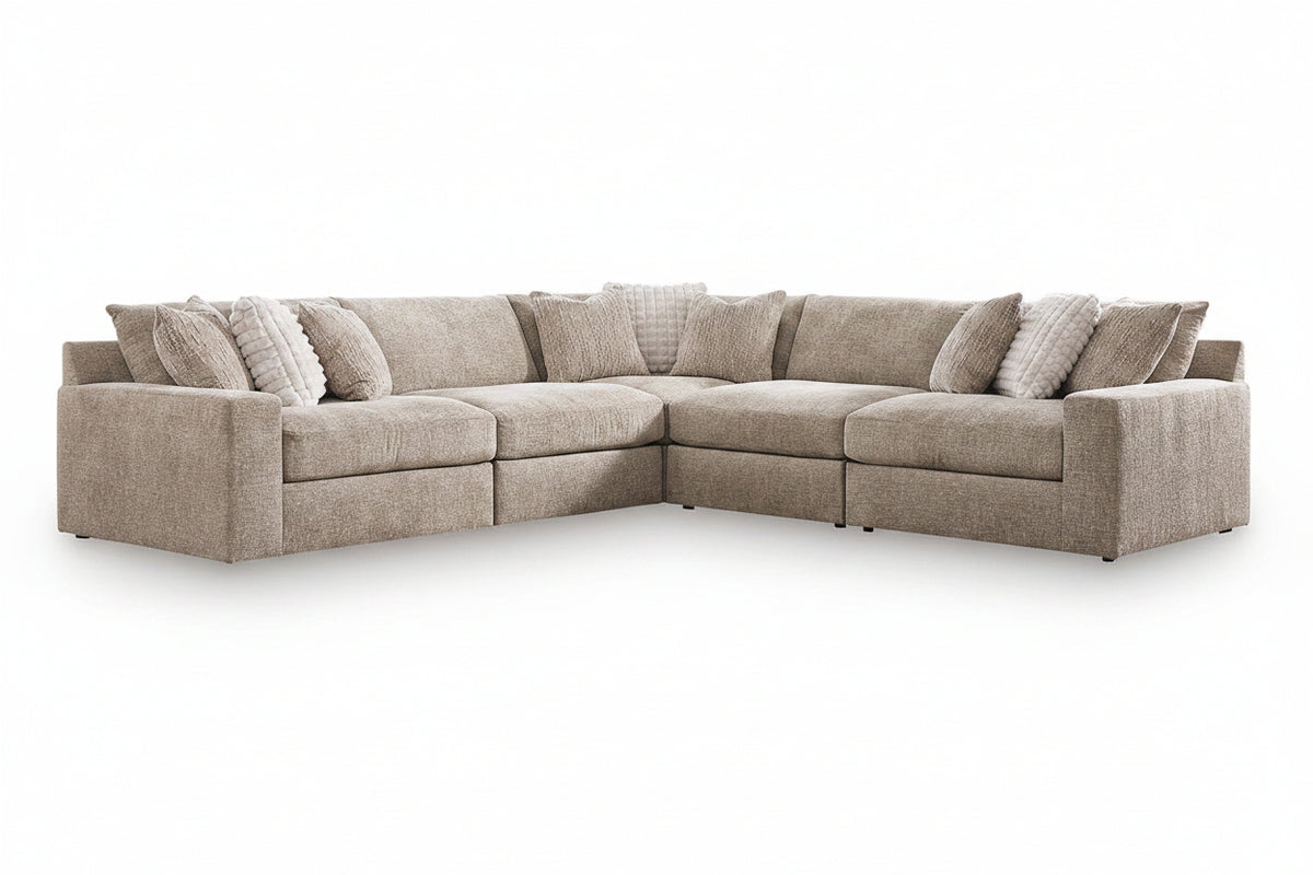 An L-shaped upholstered sofa in a textured light beige fabric, styled with multiple matching and striped accent pillows, shown on a clean white background.