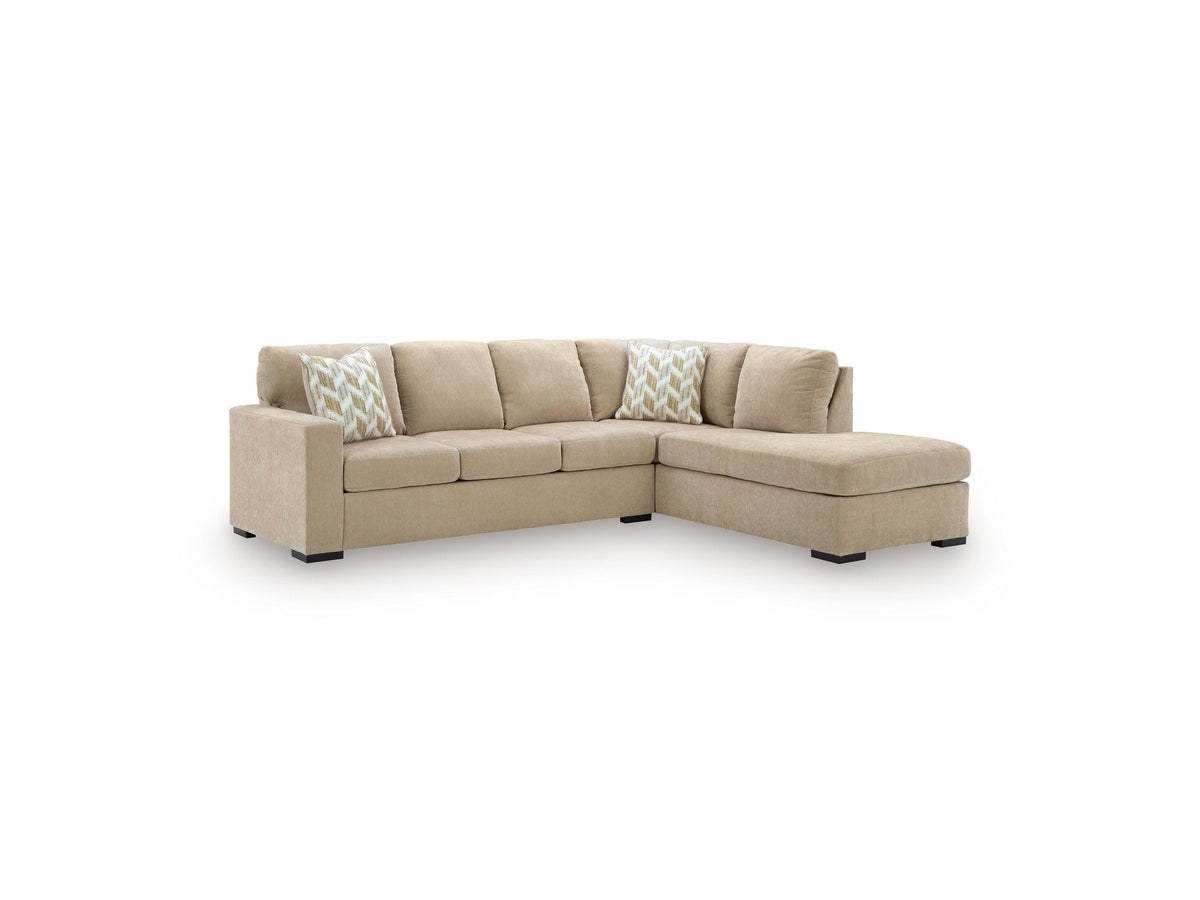 A beige fabric sectional sofa with a right-facing chaise lounge and two decorative throw pillows featuring a white and beige chevron pattern, shown against a plain white background.