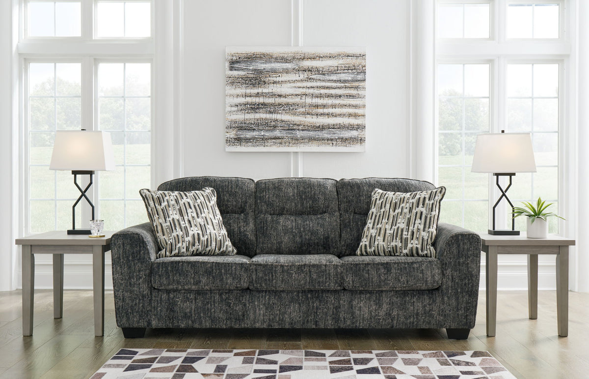 Gray sofa with patterned cushions in a living room setting with two side tables and lamps.