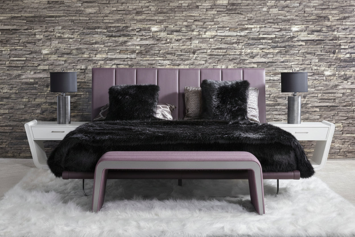 Zina modern bedroom has a purple bed and a black fur throw against a stone wall.