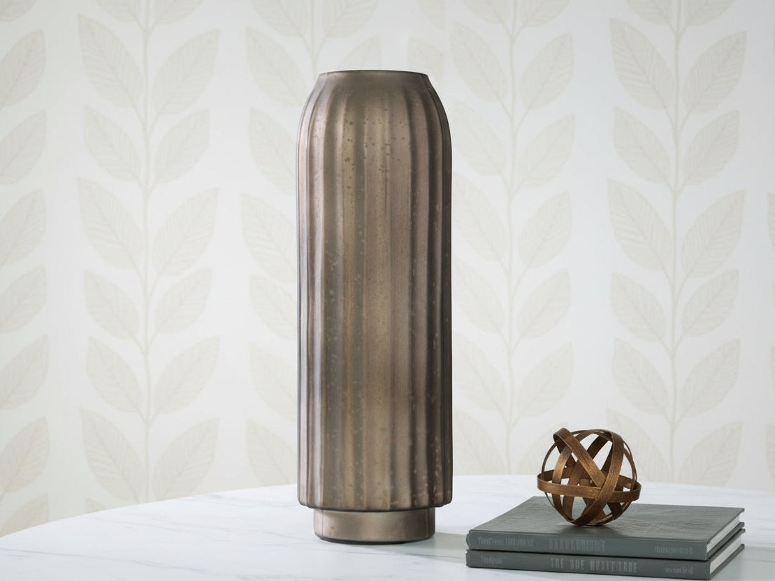 Bronze-colored vase on a light surface with a patterned wall in the background