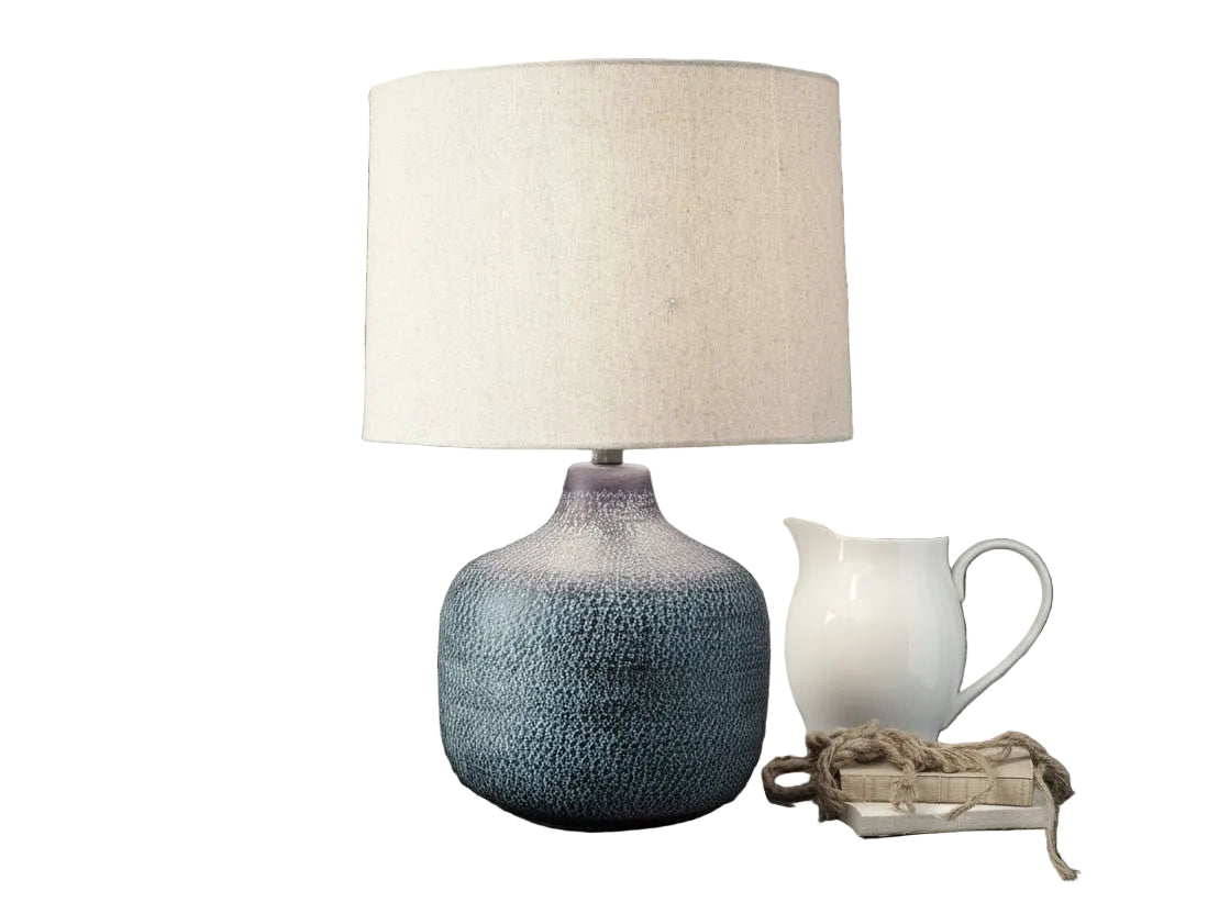 Decorative lamp with textured blue base and white shade on a wooden surface with a rustic background.