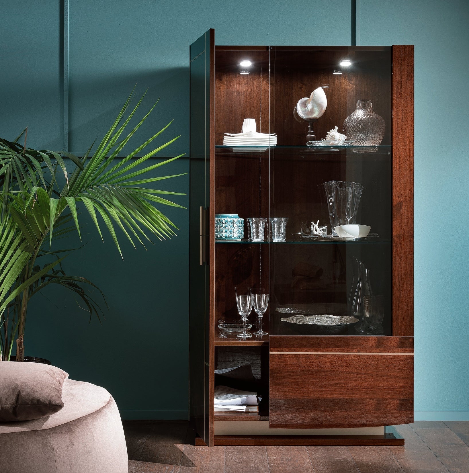 Bellagio 2-door curio with glass doors against a teal wall, featuring decorative items.