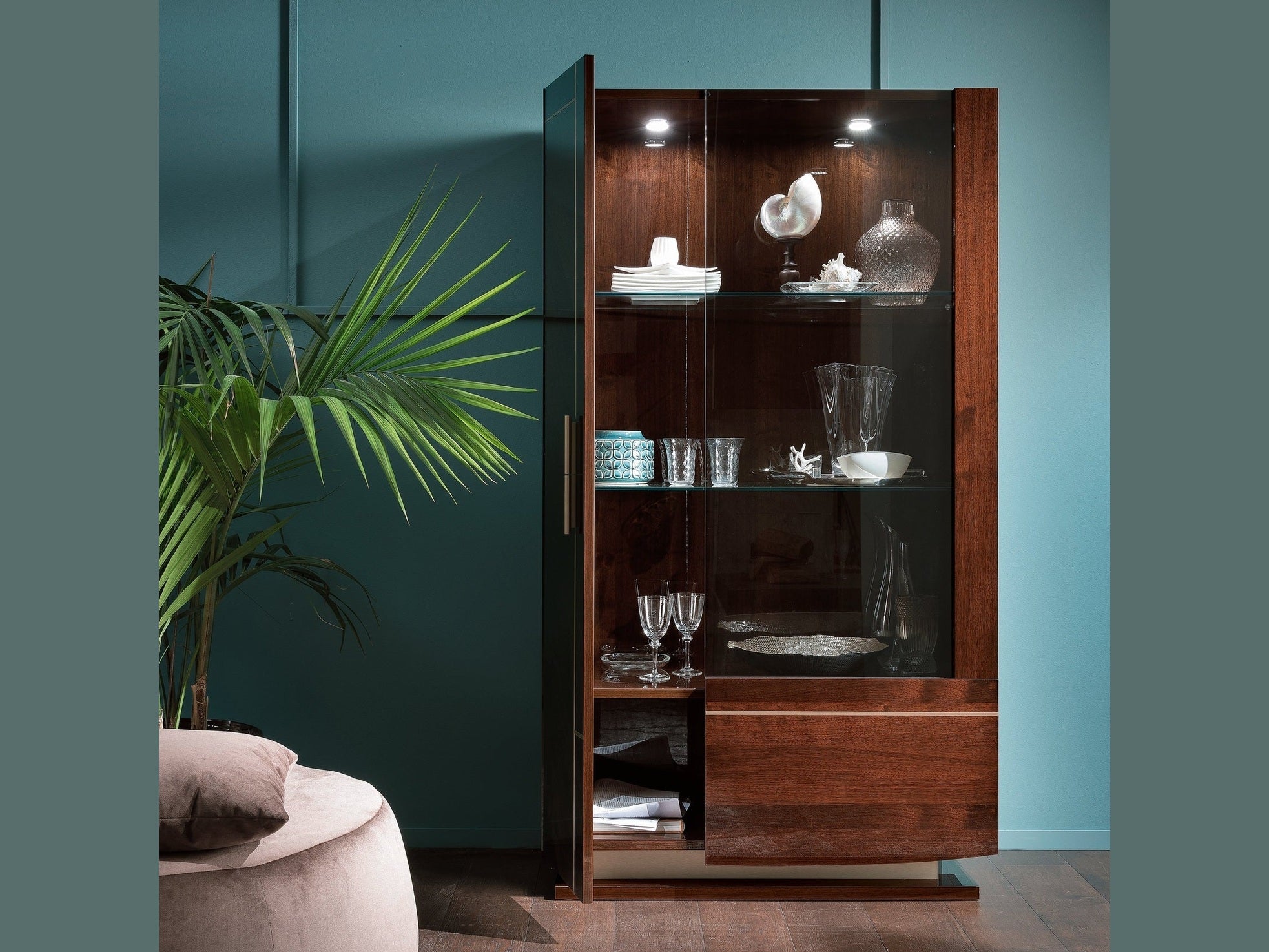 Bellagio 2-door curio with glass doors against a teal wall, featuring decorative items.