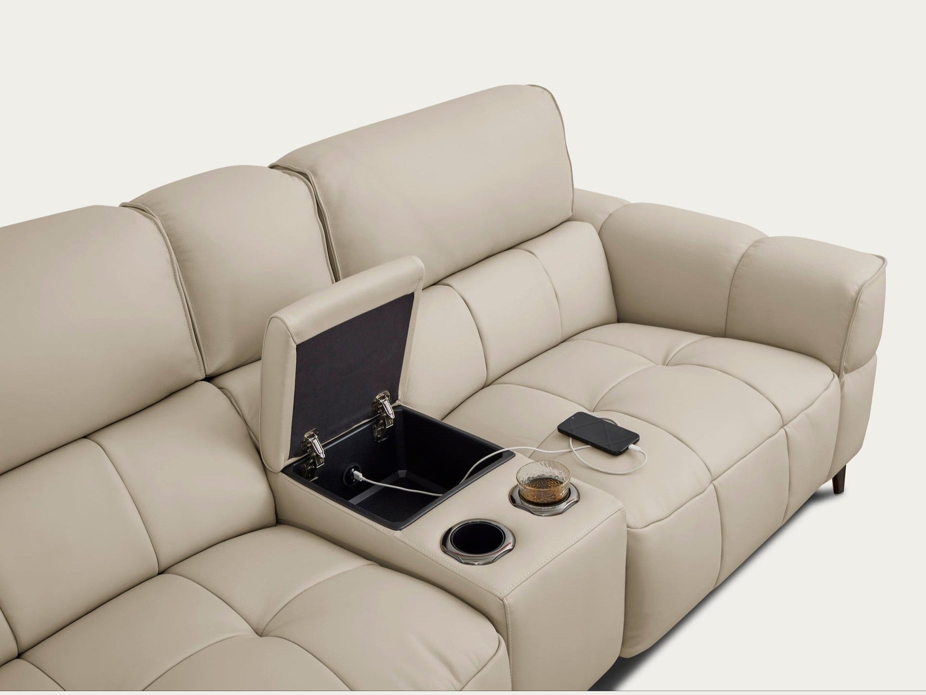 A cream leather sectional sofa showcases a functional center console with two cup holders and an open storage compartment featuring a built-in USB port charging a smartphone.