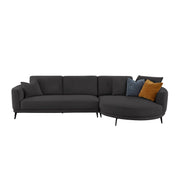 A modern dark gray sectional sofa with a left-facing armrest and a right-facing curved chaise, styled with three accent pillows in blue and mustard yellow, set against a plain light gray background.