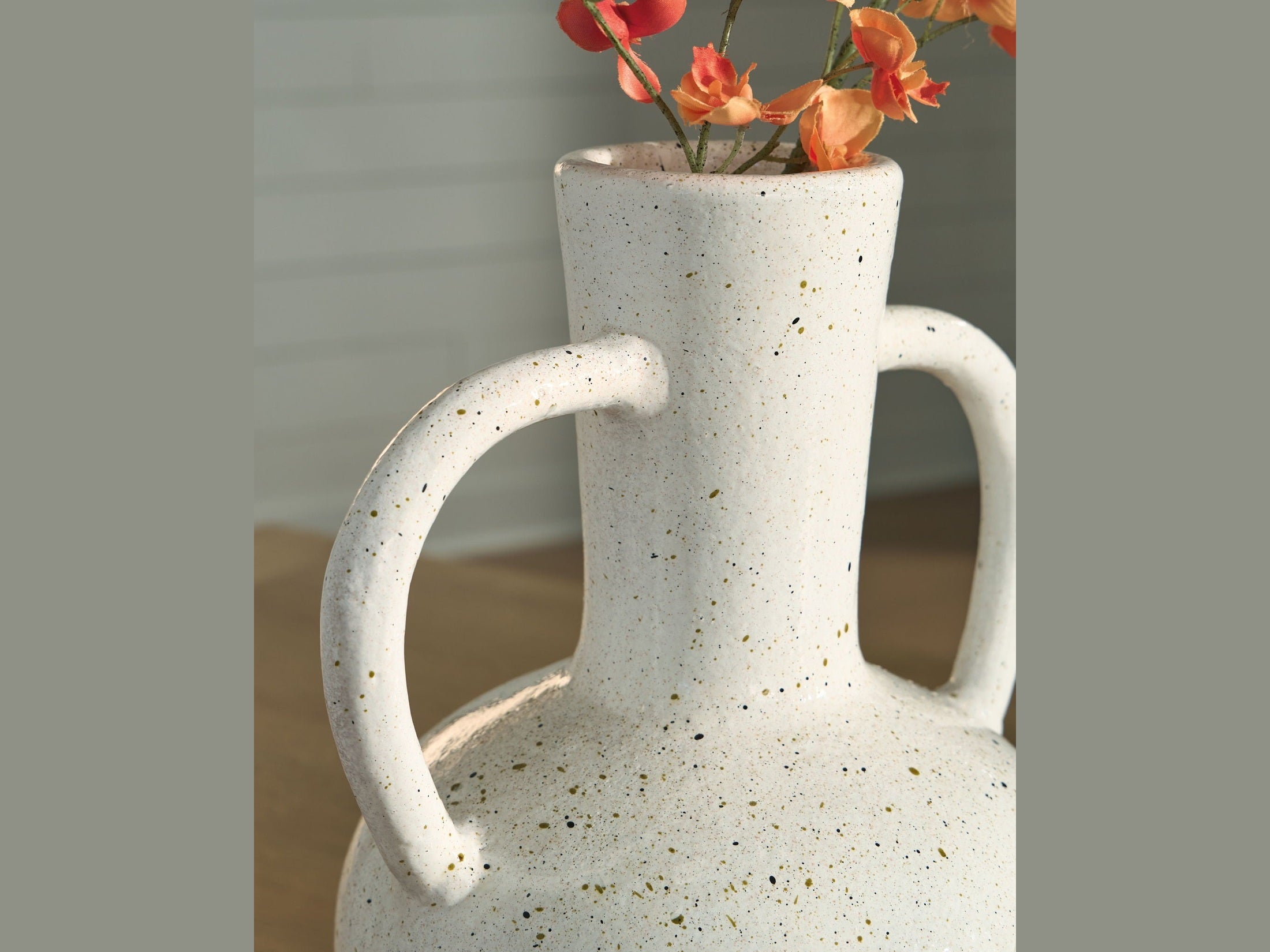 Speckled ceramic pitcher with handles holding flowers against a neutral background