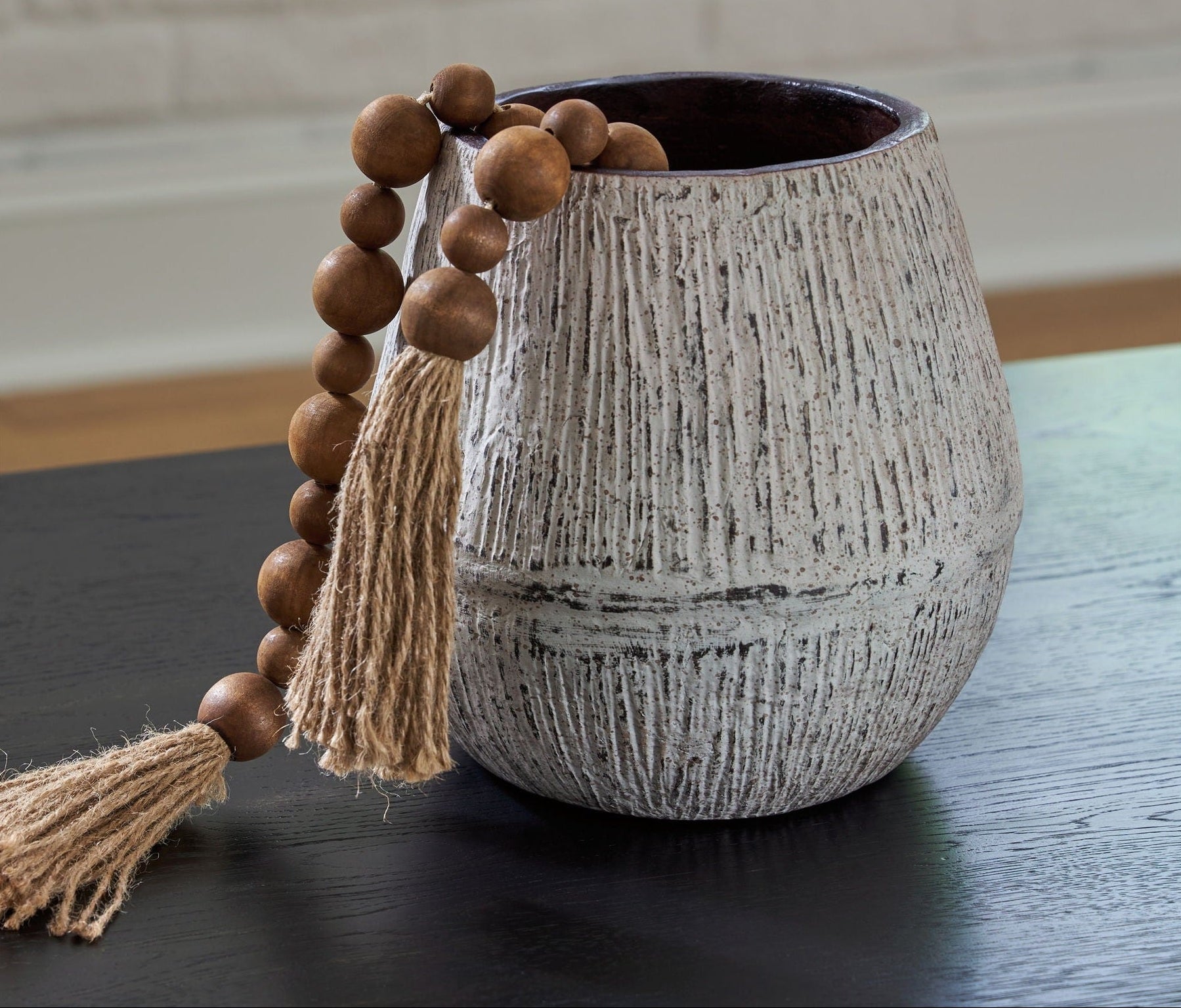 Textured vase with wooden beads and tassels on a dark surface