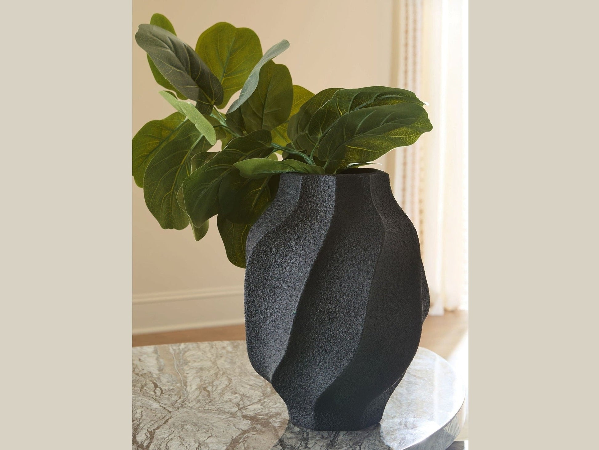 Black textured vase with green plant on a marble surface