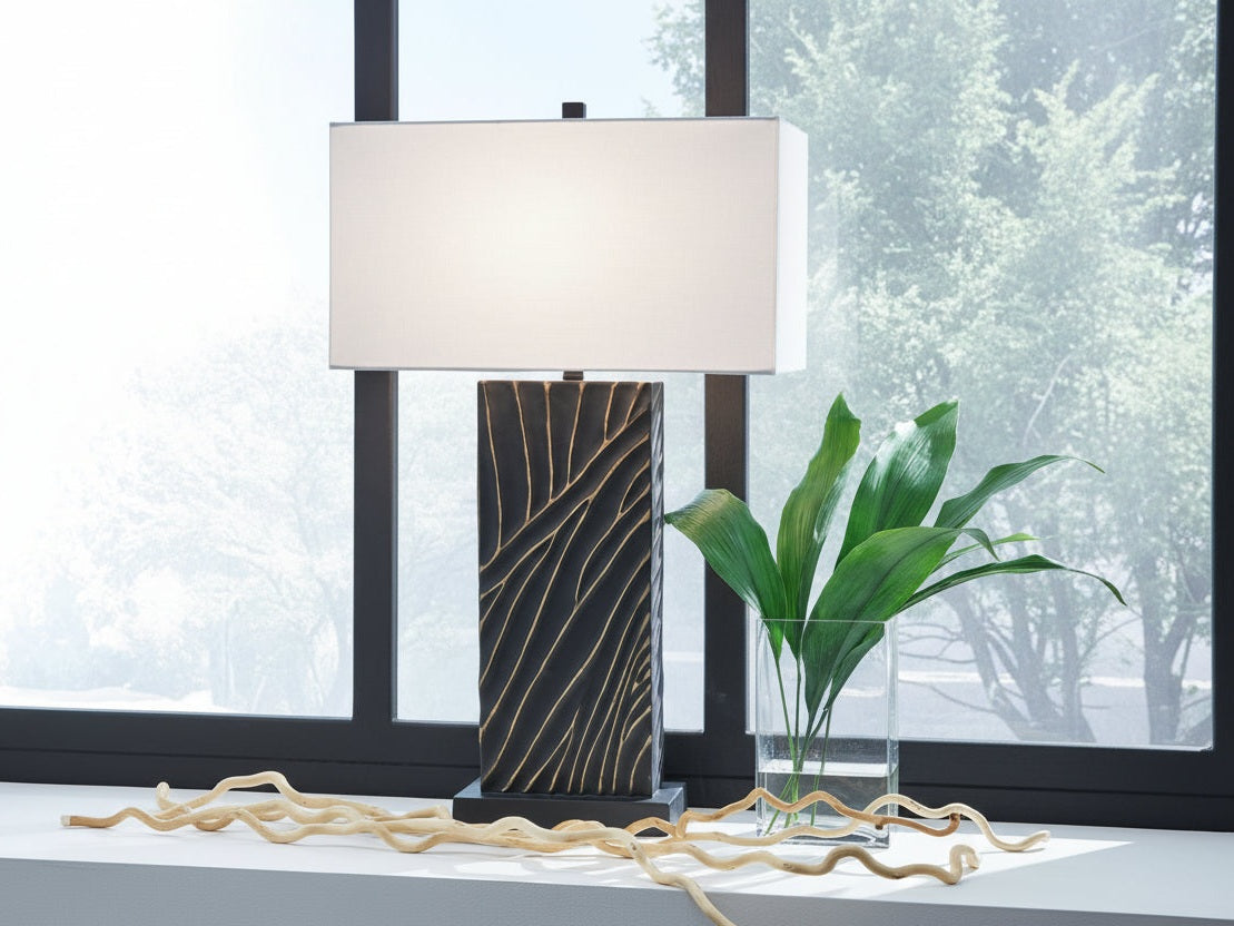 Table lamp with a decorative base and white shade on a surface near a window.